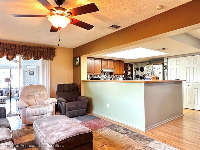 living room featuring ceiling fan, light hardwood / wood-style floors, and a textured ceiling