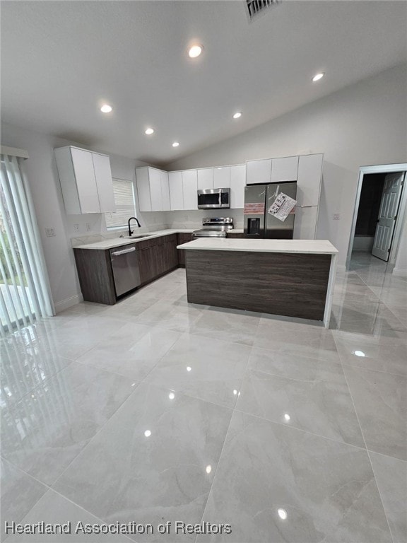 kitchen featuring dark brown cabinetry, stainless steel appliances, vaulted ceiling, white cabinetry, and an island with sink