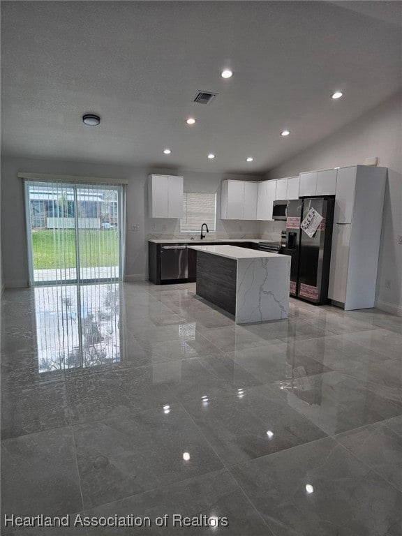 kitchen with appliances with stainless steel finishes, vaulted ceiling, sink, a center island, and white cabinetry