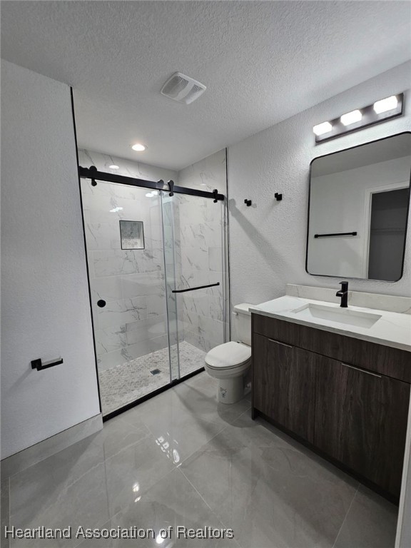 bathroom with vanity, toilet, a shower with door, and a textured ceiling