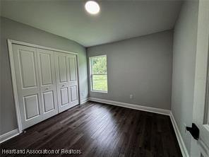 unfurnished bedroom with dark wood finished floors, baseboards, and a closet