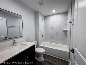 bathroom featuring wood finished floors, visible vents, toilet, vanity, and tub / shower combination