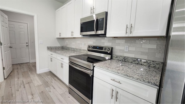 kitchen featuring light stone countertops, appliances with stainless steel finishes, tasteful backsplash, light hardwood / wood-style floors, and white cabinetry