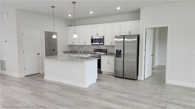 kitchen featuring a kitchen island with sink, hanging light fixtures, light stone countertops, appliances with stainless steel finishes, and white cabinetry