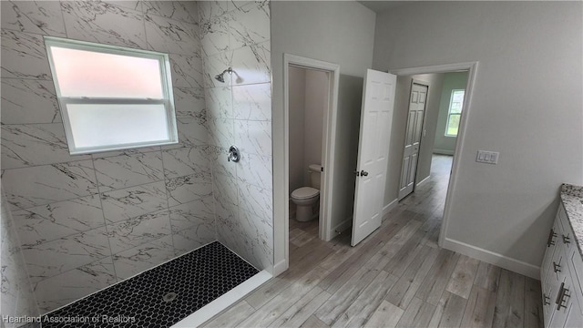 bathroom with tiled shower, wood-type flooring, vanity, and toilet