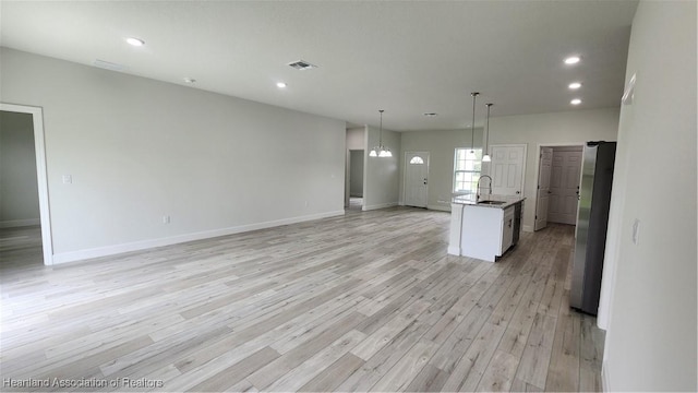 kitchen featuring sink, hanging light fixtures, stainless steel fridge, a center island with sink, and white cabinets