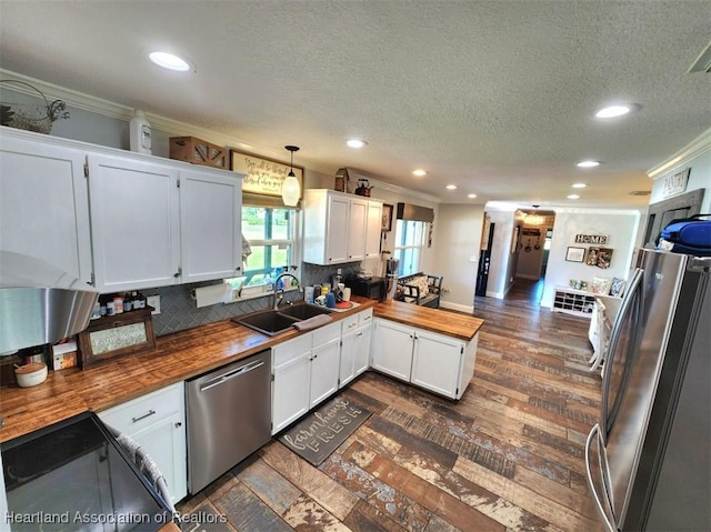 kitchen featuring butcher block counters, hanging light fixtures, sink, appliances with stainless steel finishes, and white cabinetry