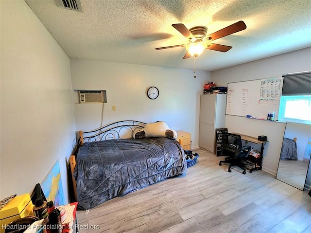 bedroom featuring ceiling fan, light wood-type flooring, a textured ceiling, and a wall mounted AC