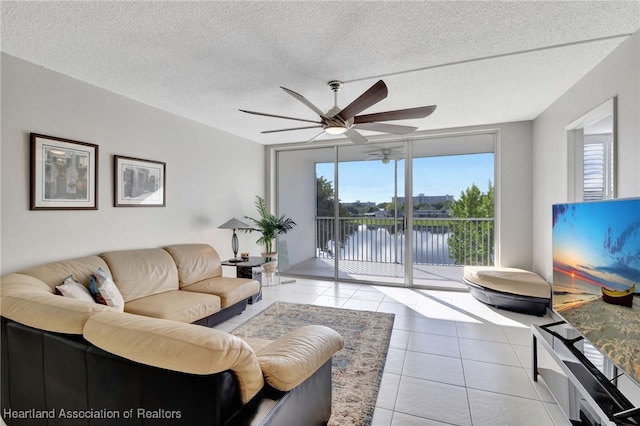 tiled living room featuring a water view, expansive windows, ceiling fan, and a textured ceiling