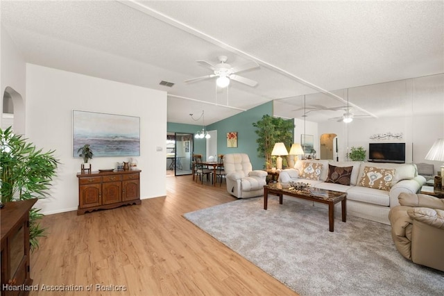 living room featuring ceiling fan with notable chandelier, a textured ceiling, and light wood-type flooring