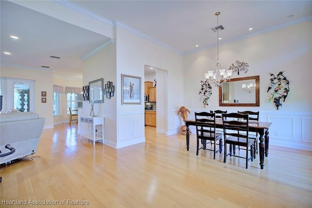 dining space featuring light wood-type flooring, visible vents, a decorative wall, and ornamental molding