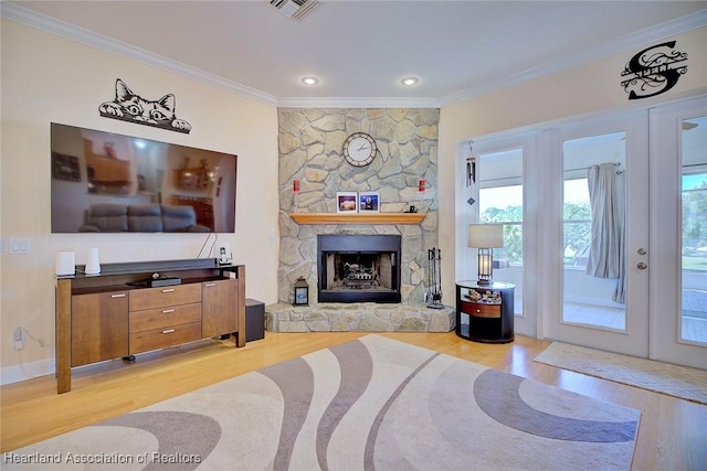 living room with french doors, visible vents, ornamental molding, light wood-style floors, and a stone fireplace