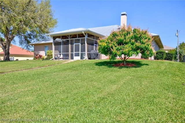 rear view of property featuring a lawn, a chimney, and a sunroom