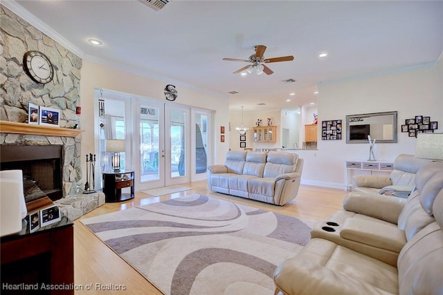 living area featuring ceiling fan with notable chandelier, ornamental molding, a fireplace, and light wood-style floors