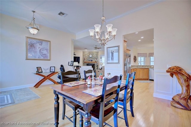 dining area featuring a large fireplace, visible vents, light wood-style floors, and ornamental molding