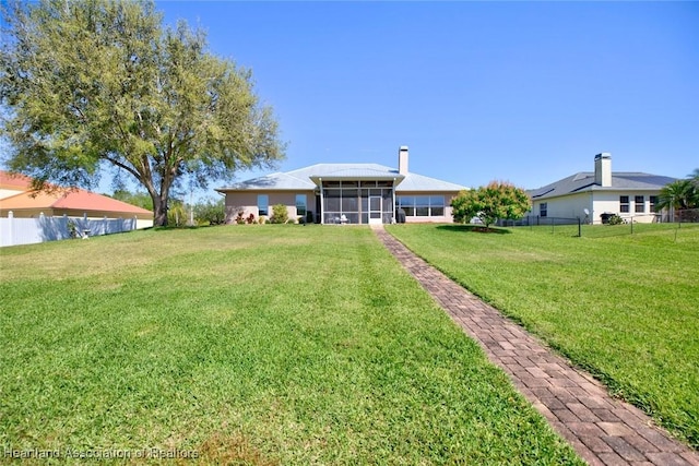 view of front of house with a front lawn, a chimney, fence private yard, and a sunroom