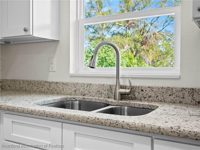 interior details featuring light stone counters, white cabinetry, and sink