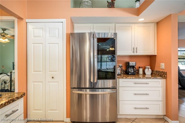 kitchen with white cabinetry, ceiling fan, stainless steel fridge, and dark stone countertops