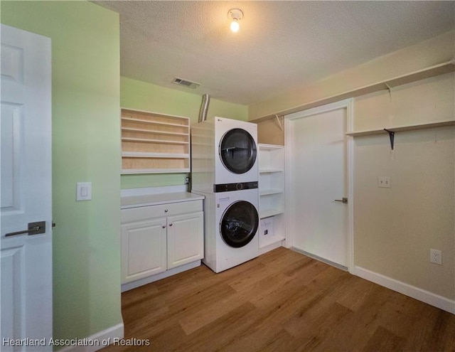 956 Shamrock Dr, Sebring, FL 33875 - laundry room with stacked washer / drying machine, cabinet space, wood finished floors, a textured ceiling, and baseboards