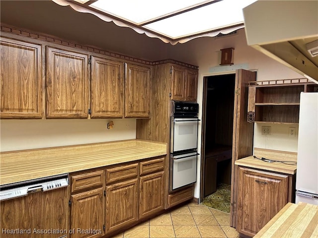 kitchen with dishwasher, light tile patterned floors, white refrigerator, and multiple ovens