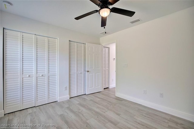 unfurnished bedroom with visible vents, baseboards, multiple closets, wood finished floors, and a ceiling fan