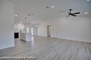 unfurnished living room featuring recessed lighting, baseboards, lofted ceiling, and light wood-style flooring