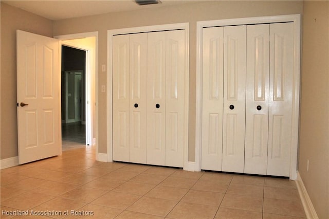 unfurnished bedroom with light tile patterned floors and two closets