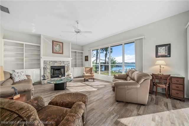 living room with ceiling fan, a water view, built in features, hardwood / wood-style flooring, and a fireplace