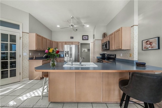 kitchen with kitchen peninsula, a kitchen bar, stainless steel appliances, sink, and light tile patterned flooring