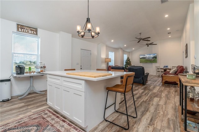 kitchen with ceiling fan with notable chandelier, pendant lighting, white cabinets, a kitchen island, and lofted ceiling