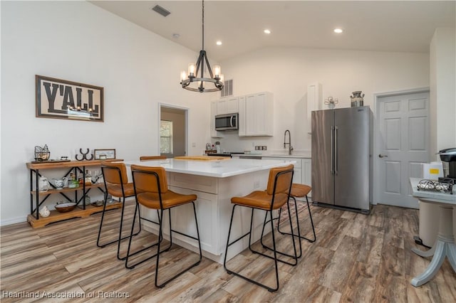 kitchen featuring stainless steel appliances, an inviting chandelier, white cabinets, light hardwood / wood-style flooring, and a kitchen island