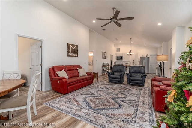 living room with light wood-type flooring, ceiling fan with notable chandelier, and high vaulted ceiling