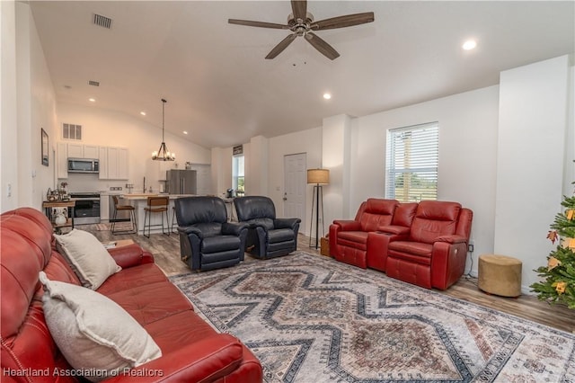 living room with ceiling fan with notable chandelier, light wood-type flooring, and vaulted ceiling