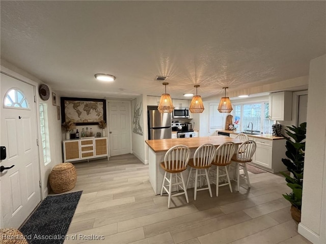 kitchen featuring a breakfast bar, light hardwood / wood-style flooring, appliances with stainless steel finishes, decorative light fixtures, and white cabinetry