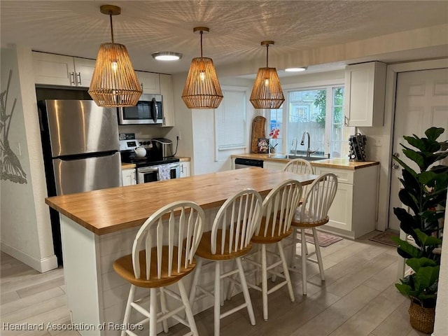 kitchen featuring butcher block counters, white cabinetry, stainless steel appliances, decorative light fixtures, and a kitchen island