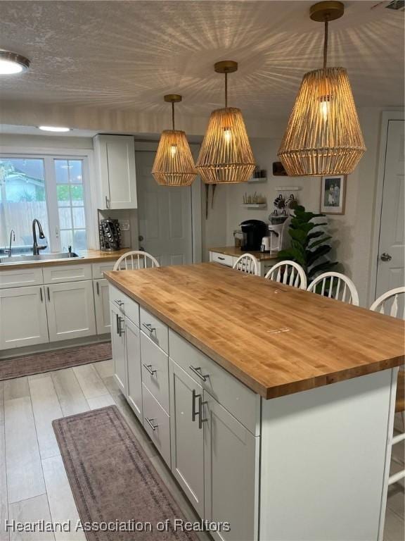 kitchen with wood counters, a center island, white cabinets, sink, and hanging light fixtures