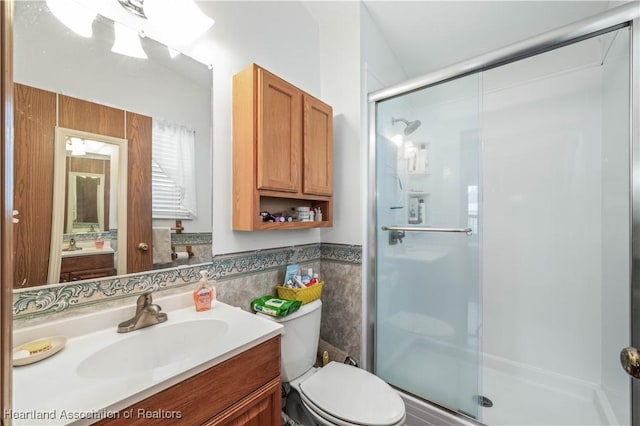 bathroom featuring vanity, toilet, a shower with door, and tile walls