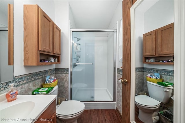 bathroom featuring wood-type flooring, toilet, vanity, a shower with shower door, and tile walls