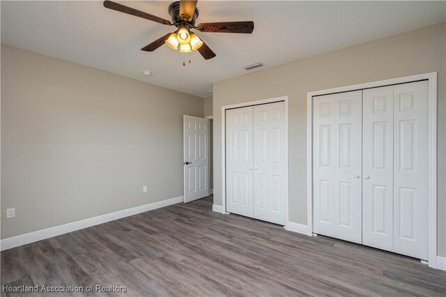 unfurnished bedroom featuring hardwood / wood-style floors, ceiling fan, and multiple closets