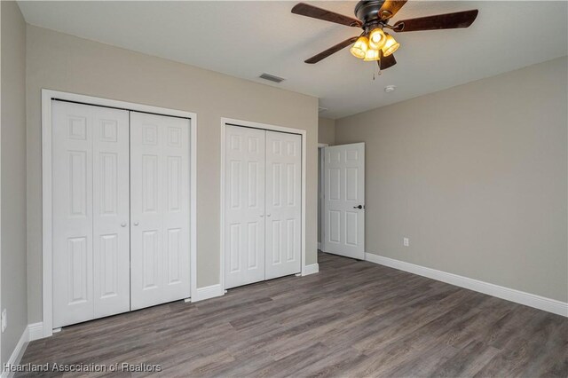 unfurnished bedroom featuring hardwood / wood-style flooring, ceiling fan, and multiple closets