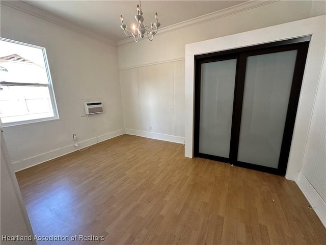 spare room featuring a wall mounted air conditioner, ornamental molding, hardwood / wood-style flooring, and an inviting chandelier