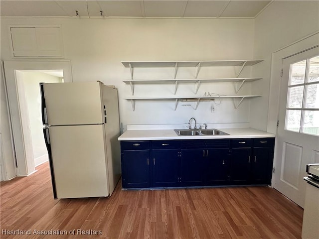 kitchen featuring hardwood / wood-style flooring, white fridge, blue cabinetry, and sink