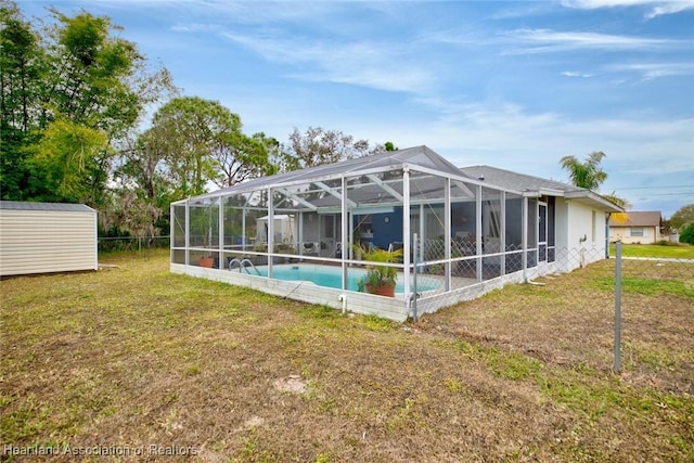 rear view of property with glass enclosure, a yard, and a storage unit