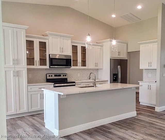 kitchen with white cabinets, appliances with stainless steel finishes, decorative light fixtures, an island with sink, and sink