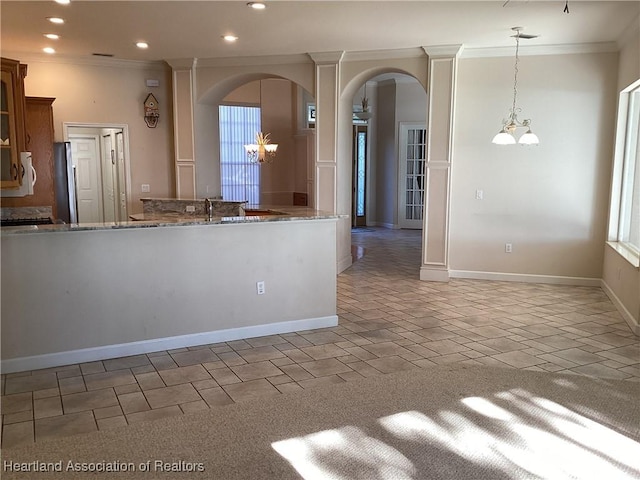 kitchen with hanging light fixtures, light stone counters, crown molding, stainless steel fridge, and a chandelier