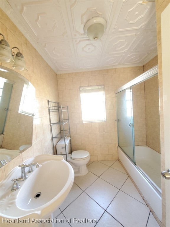 bathroom with tile patterned flooring, an ornate ceiling, tile walls, and a sink