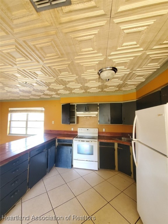 kitchen featuring white appliances, light tile patterned floors, dark countertops, an ornate ceiling, and under cabinet range hood