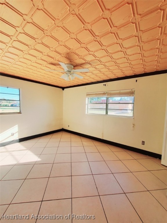 spare room with light tile patterned floors, ornamental molding, an ornate ceiling, and baseboards