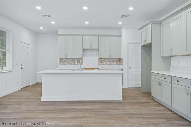 kitchen featuring a kitchen island with sink, decorative backsplash, gray cabinetry, and light hardwood / wood-style floors