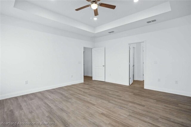 empty room featuring ceiling fan, hardwood / wood-style floors, and a tray ceiling